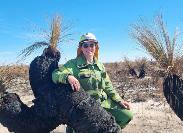 Kayla sit next to a small burnt tree. Kayla is wearing her green overall