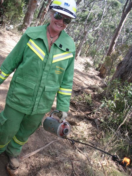 Firefighter in green uniform holds a drip torch