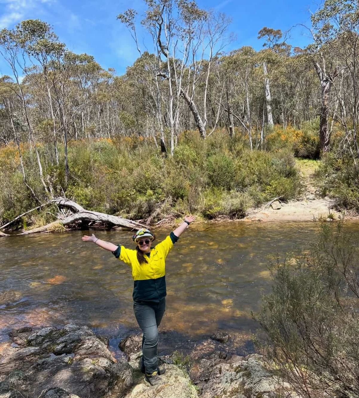Lara standing beside a creek with her arms in the air
