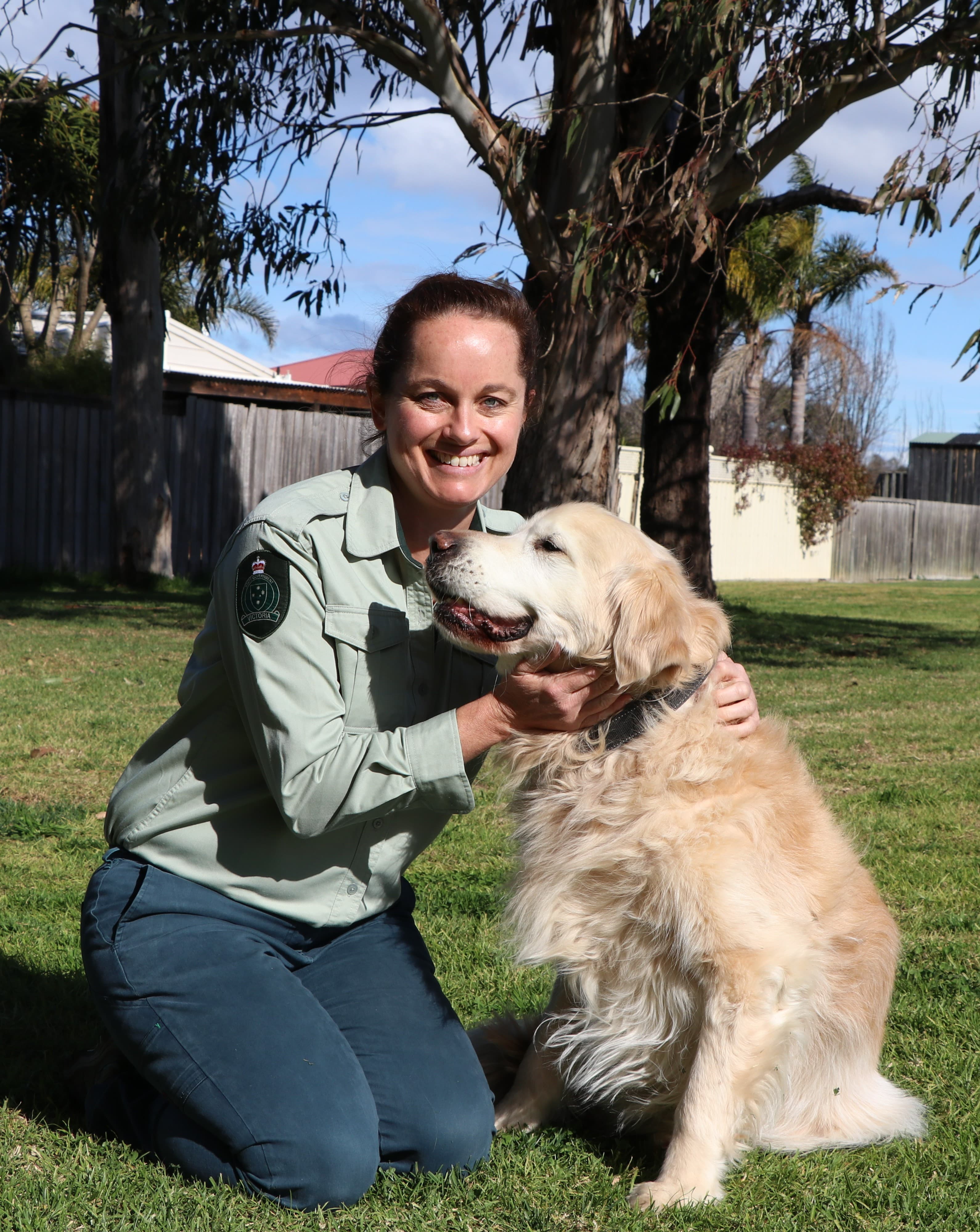 Kate Biles crouching down and patting her Golden Retriever named Otis.