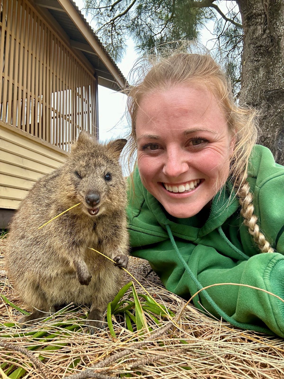 A woman in a green fire uniform poses with a quokka