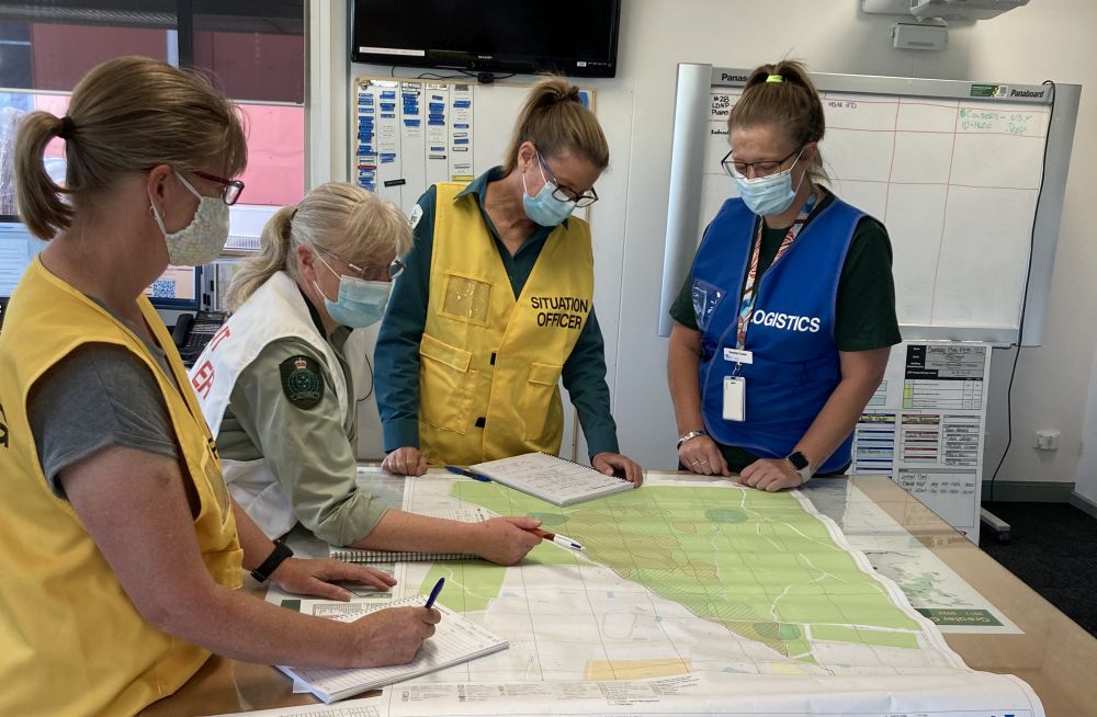 Four people in coloured vests stand at a table with fire maps