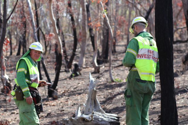 Two fire investigators wearing their green overalls, inspecting a burnt site.