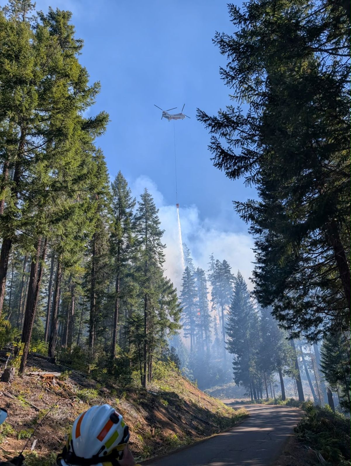 A white and red helicopter dropping water into the wildfire zone